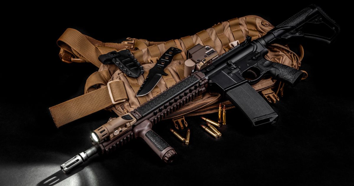 A rifle with a tactical light one and other shooting gear laying against a black background.