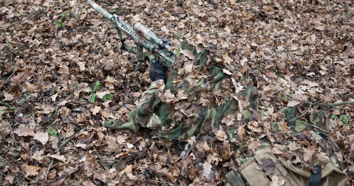 A sniper covered in leaves and camouflage.