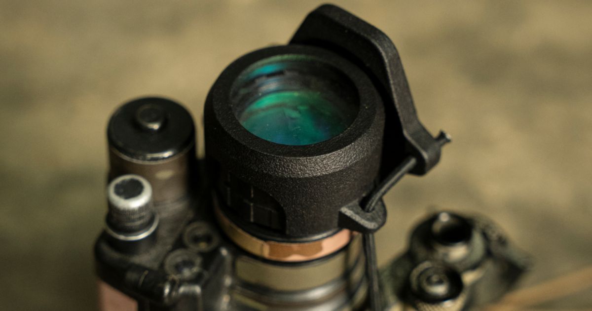 A close-up of a rifle scope with a scope cap from One Hundred Concepts.