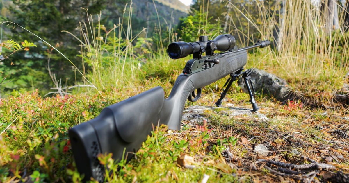 A long-range precision rifle sitting in the grass on a bipod.