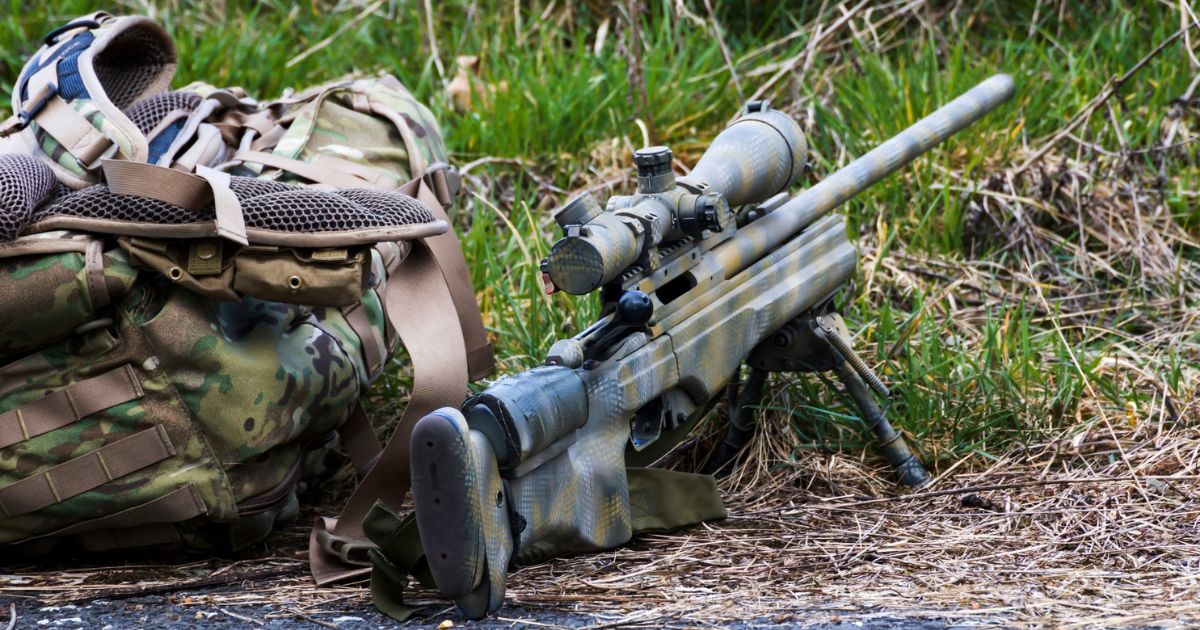 A long distance shooting rilfe next to a gear pack.
